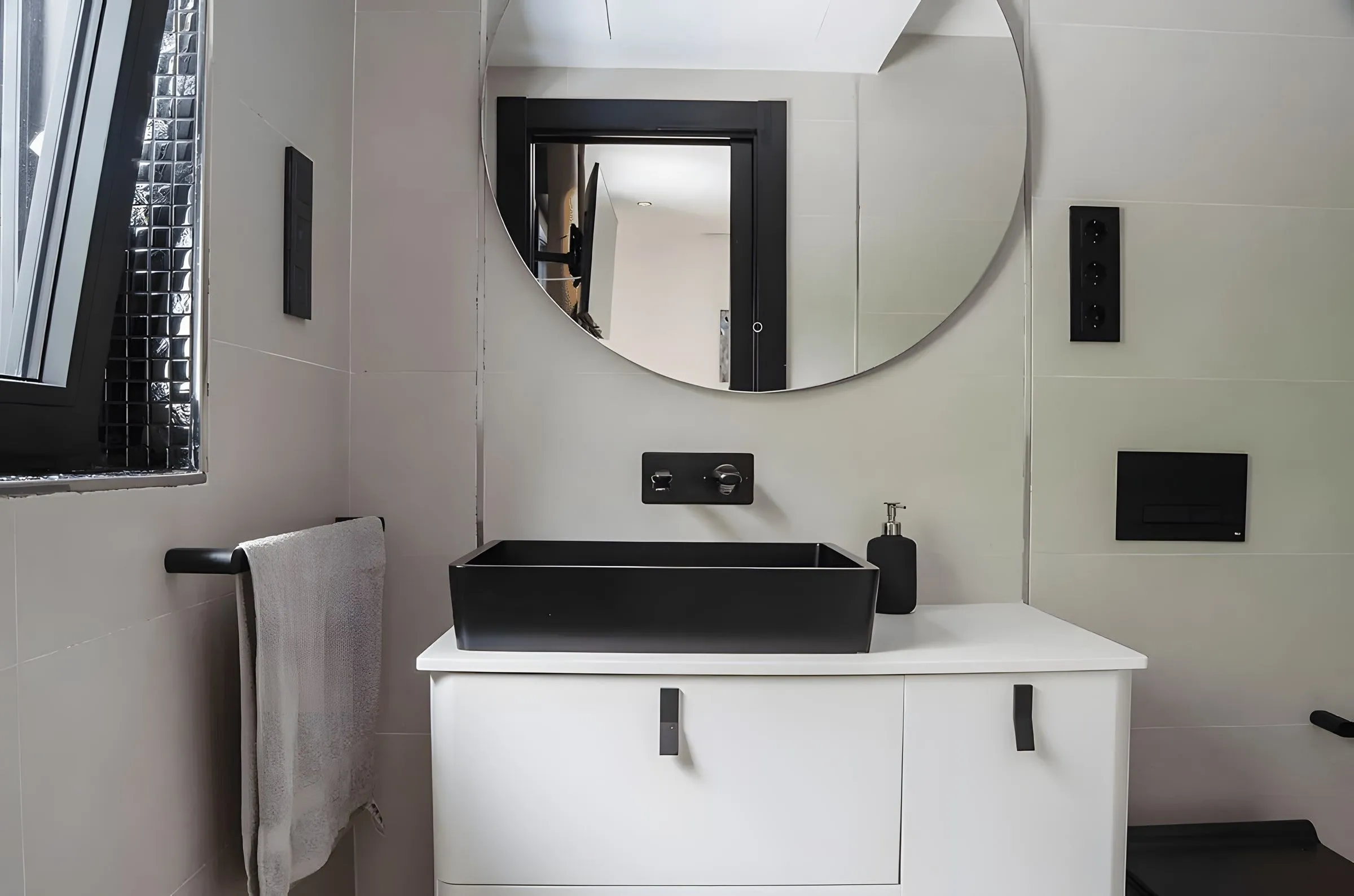 Baño de invitados con lavabo negro y espejo redondo